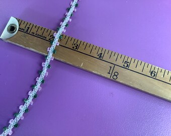 May include: A close-up of a pink and green trim with a ruler measuring 4 and 1/8 inches. The trim is made of a delicate fabric with small flowers and leaves.