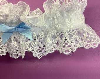 May include: White lace garter with a light blue bow. The garter is made of delicate lace and has a ruffled edge.