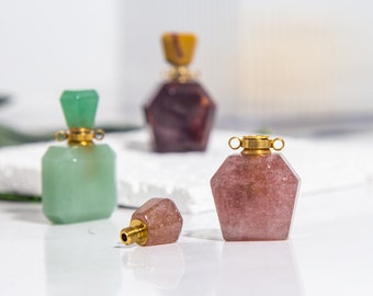 May include: Three small gemstone bottles with gold caps. The bottles are green, pink, and purple. The bottles are on a white surface.