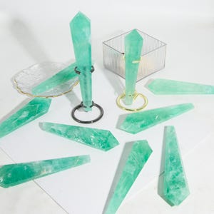 May include: A collection of green fluorite crystal wands on a white surface. The wands are various sizes and shapes, with some on stands.