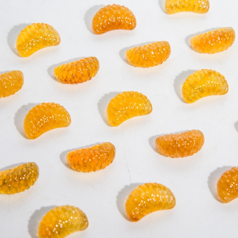 Puede incluir: Una colecci&oacute;n de peque&ntilde;os segmentos de color naranja transl&uacute;cido dispuestos en un patr&oacute;n de cuadr&iacute;cula. Cada pieza presenta una superficie texturizada y curva que imita la apariencia de secciones de c&iacute;tricos, en un tono &aacute;mbar brillante.