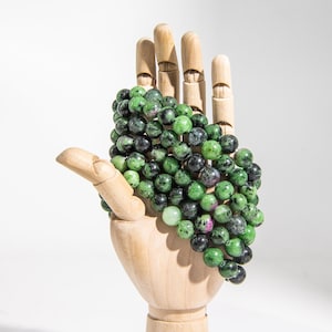 Puede incluir: Un hilo de cuentas de piedras preciosas verdes y negras, probablemente de aventurina verde, en una mano de madera.