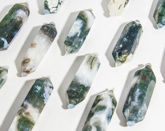 May include: A collection of double-terminated moss agate crystal points, each featuring unique green and white dendritic inclusions. These polished stone wands are arranged in a grid, showcasing natural patterns of translucent white quartz and deep green moss-like mineral formations.