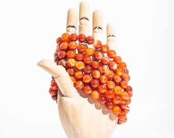 May include: A strand of carnelian beads with white stripes, displayed on a wooden hand.