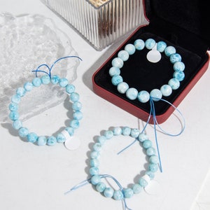 Könnte beinhalten: Drei blaue und weiße Edelstein-Armbänder mit blauen Schnüren. Die Armbänder bestehen aus runden Perlen und werden auf einer weißen Oberfläche präsentiert.