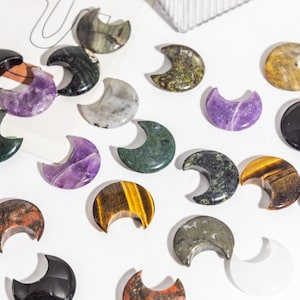 Peut inclure: Une collection de pierres polies en forme de croissant de lune de différentes couleurs et motifs, notamment l'améthyste, l'œil de tigre, l'aventurine verte et l'obsidienne noire.