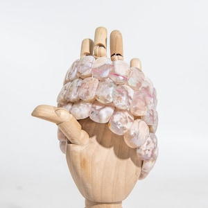 Puede incluir: Un maniquí de mano de madera que lleva una pulsera hecha de piedras de ágata rosa y blanca. Las piedras tienen una forma irregular y una apariencia natural y nublada.