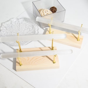 May include: Three clear, cylindrical crystal wands displayed on wooden bases with gold-colored metal supports. A clear plastic container with decorative balls and a clear, irregular-shaped object are in the background. The wands are approximately 10 inches long.