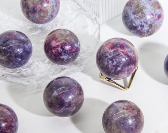 May include: A collection of eight purple and pink gemstone spheres, some on a clear glass plate and others on a gold stand. The spheres have a swirling, marbled pattern.