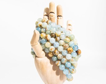 May include: A multi-strand bracelet made of blue and brown agate beads. The beads are round and have a smooth, polished finish. The bracelet is displayed on a wooden hand.