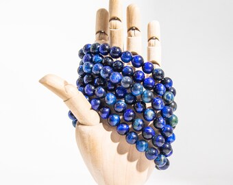 Pode incluir: Um bracelete de contas de olho de tigre azul em uma mão de madeira.
