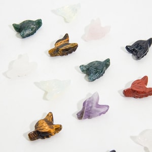Könnte beinhalten: Eine Sammlung von 11 Wolfskopf-Schnitzereien aus verschiedenen Edelsteinen, darunter Amethyst, Tigerauge, Rosenquarz und grüner Aventurin.