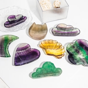 May include: A set of eight colorful fluorite crystal carvings in various shapes, including a heart, a crescent moon, a cloud, a cat, and a seashell. The carvings are made of natural fluorite, which is known for its vibrant colors and unique patterns.