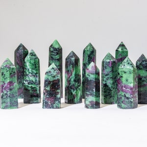 May include: A collection of green and purple gemstone points, also known as zoisite, arranged in a row on a white surface.