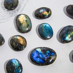 May include: A collection of ten smooth, oval-shaped labradorite stones. The stones are a mix of dark blue, green, and gold colors with iridescent shimmer.