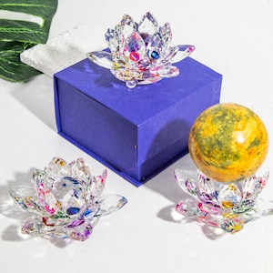 May include: Three crystal lotus flower bases, one with a yellow and green sphere on top. The bases are clear with iridescent accents and are displayed on a purple box.