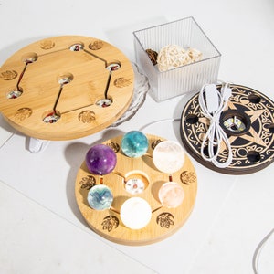 May include: A selection of wooden crystal sphere display bases with LED lights. The bases are round with different designs, including a Celtic knot and lotus flower. The spheres are in shades of purple, blue, and white.
