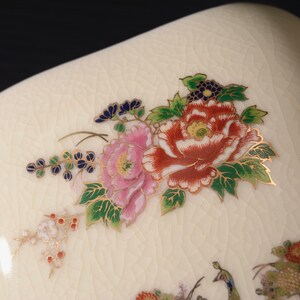 May include: A white ceramic dish with a floral design. The flowers are pink, red, and green with gold accents. The dish has a textured surface.
