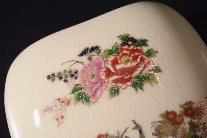 May include: A white ceramic dish with a floral design. The flowers are pink, red, and green with gold accents. The dish has a textured surface.