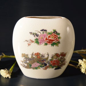 May include: White ceramic vase with a floral design featuring pink, red, and yellow flowers. The vase has a textured surface and a gold rim.