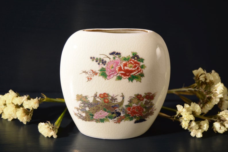 May include: White ceramic vase with a floral design featuring pink, red, and yellow flowers. The vase has a textured surface and a gold rim.