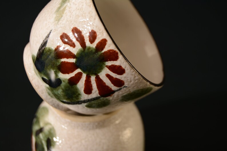 Puede incluir: Dos cuencos de cer&aacute;mica blanca con un dise&ntilde;o floral. Los cuencos est&aacute;n apilados uno encima del otro. El dise&ntilde;o presenta flores rojas, verdes y negras.