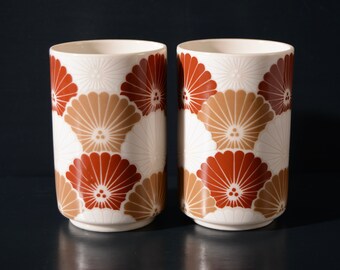 Puede incluir: Dos tazas de cerámica blanca con un patrón floral marrón y rojo. Las tazas tienen una forma redondeada y un interior blanco.