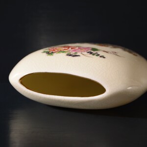 May include: A white ceramic vase with a floral design and a gold rim. The vase has a wide opening and a rounded shape.
