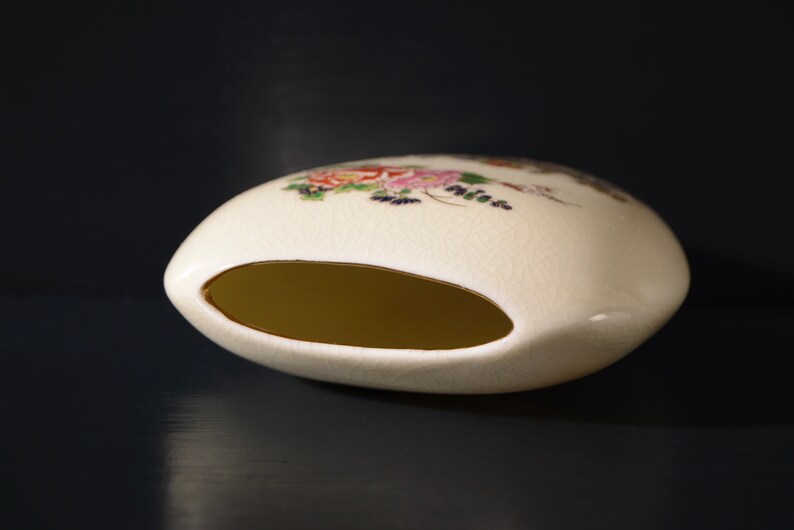 May include: A white ceramic vase with a floral design and a gold rim. The vase has a wide opening and a rounded shape.