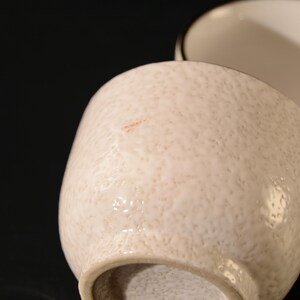 Puede incluir: Dos tazas de t&eacute; de cer&aacute;mica blanca con una superficie texturizada. Una taza tiene un dise&ntilde;o de hoja verde.