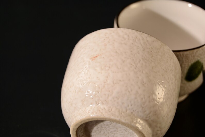 Puede incluir: Dos tazas de t&eacute; de cer&aacute;mica blanca con una superficie texturizada. Una taza tiene un dise&ntilde;o de hoja verde.