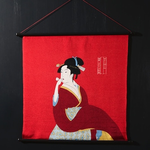 May include: A red fabric wall hanging with a black and white illustration of a woman in a red and blue kimono. The woman is holding a flower in her hand and has a flower in her hair. The text "春之宴" is embroidered in white on the right side of the hanging.