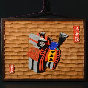 May include: A wooden plaque with a carved design of a colorful Japanese warrior figure. The plaque is framed in dark wood and has a hanging cord. The text "青海波" is written in red on the plaque.