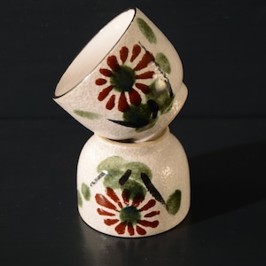 Puede incluir: Dos cuencos de cer&aacute;mica blanca con un dise&ntilde;o floral. Los cuencos est&aacute;n apilados uno encima del otro. El dise&ntilde;o presenta hojas verdes, flores marrones y detalles negros.