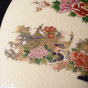 May include: A white ceramic vase with a floral and peacock design. The vase features gold accents and a textured surface.