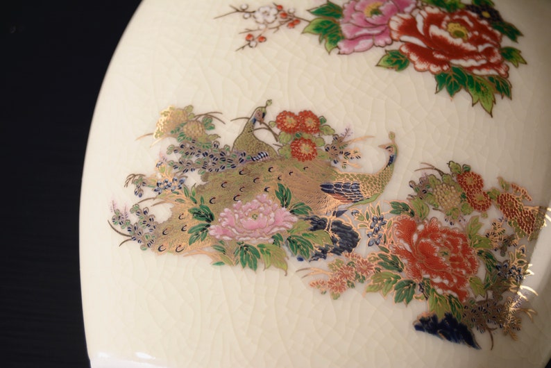 May include: A white ceramic vase with a floral and peacock design. The vase features gold accents and a textured surface.