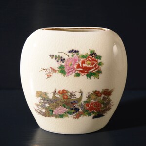 May include: A white ceramic vase with a floral design featuring pink, red, and yellow flowers, green leaves, and gold accents. The vase has a rounded oval shape.