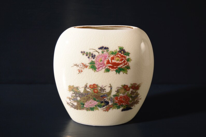 May include: A white ceramic vase with a floral design featuring pink, red, and yellow flowers, green leaves, and gold accents. The vase has a rounded oval shape.