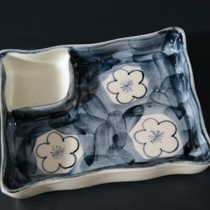 May include: A white ceramic serving dish with a blue and white floral design. The dish has a small square compartment and a larger rectangular compartment.