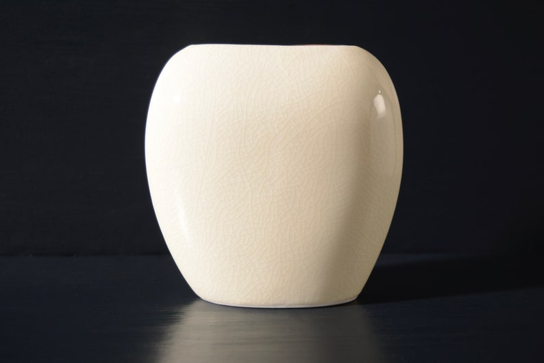 May include: A white ceramic vase with a textured surface. The vase is oval shaped and has a smooth, rounded bottom.