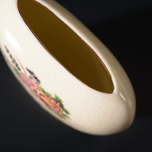 May include: A white ceramic vase with a floral design. The vase has a wide opening and a rounded shape.