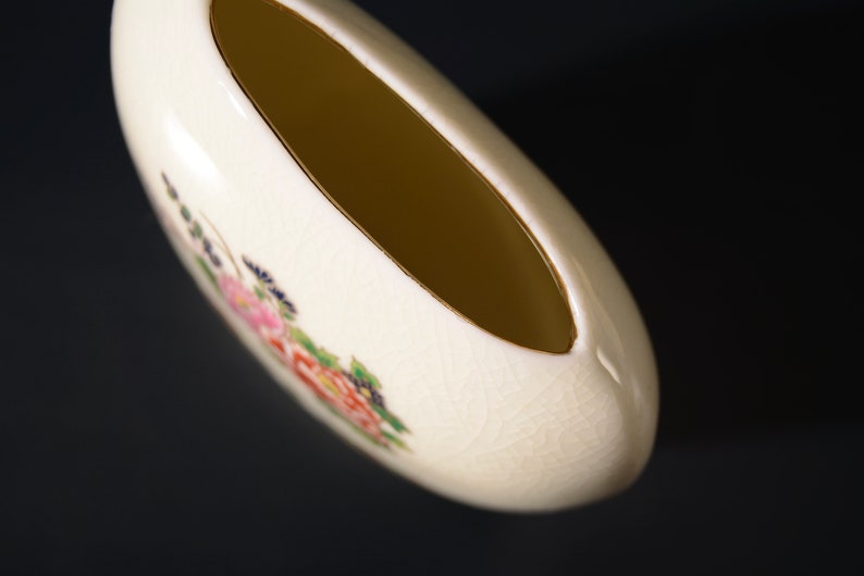 May include: A white ceramic vase with a floral design. The vase has a wide opening and a rounded shape.