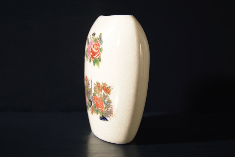 May include: White ceramic vase with a floral design. The vase is oval shaped and has a textured surface.