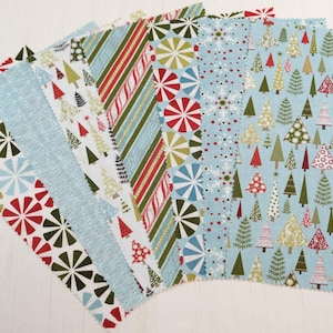 Puede incluir: Una colección de muestras de tela con motivos navideños festivos. Los diseños incluyen árboles rojos y verdes, copos de nieve y patrones de rayas en rojo, verde y blanco. Las telas son principalmente azul claro y blanco.