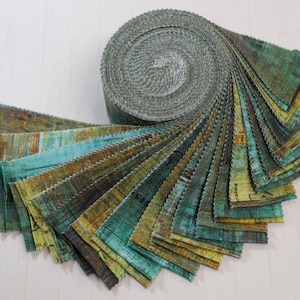May include: A fabric jelly roll featuring a collection of strips with pinked edges. The fabric displays a mottled, textured pattern in shades of teal, olive green, mustard yellow, and dark brown, with faint printed text visible on some segments.