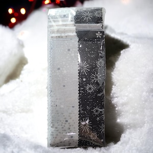 May include: A pack of fabric strips. One side of the fabric has a white and silver pattern, the other side has a black and white snowflake design. The edges are zig-zag cut. The fabric is in a clear plastic package.