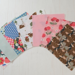 May include: A set of eight fabric squares with various patterns, including floral, polka dot, and animal prints. The squares are in shades of pink, blue, green, and brown.