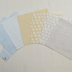 May include: A selection of seven fabric squares in a fan arrangement. The fabrics feature patterns such as geese, stripes, and dots in light blue, yellow, and grey. These are likely for crafting or quilting projects.
