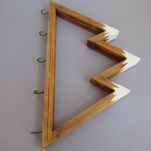 Puede incluir: Soporte para llaves de madera con dise&ntilde;o en zigzag. El soporte para llaves est&aacute; hecho de madera marr&oacute;n claro con puntas pintadas de blanco. Tiene seis peque&ntilde;os ganchos de metal para colgar llaves. El dise&ntilde;o es una forma moderna y decorativa de organizar llaves.