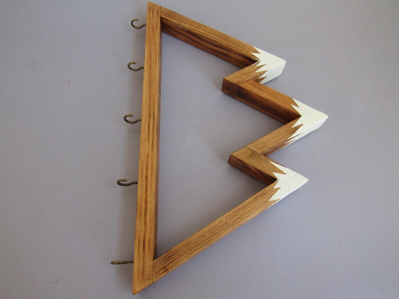 Puede incluir: Soporte para llaves de madera con dise&ntilde;o en zigzag. El soporte para llaves est&aacute; hecho de madera marr&oacute;n claro con puntas pintadas de blanco. Tiene seis peque&ntilde;os ganchos de metal para colgar llaves. El dise&ntilde;o es una forma moderna y decorativa de organizar llaves.